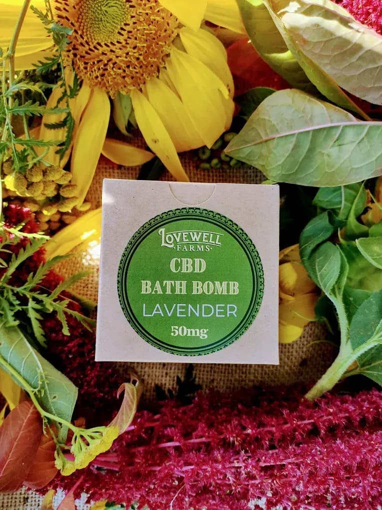 Lavender CBD bath bomb surrounded by colorful flowers and greenery.